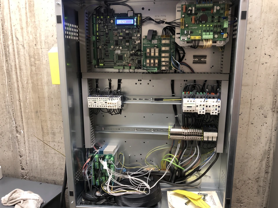 Technicien en combinaison travaillant sur panneau électrique industriel, manipulation de câbles avec outil de précision