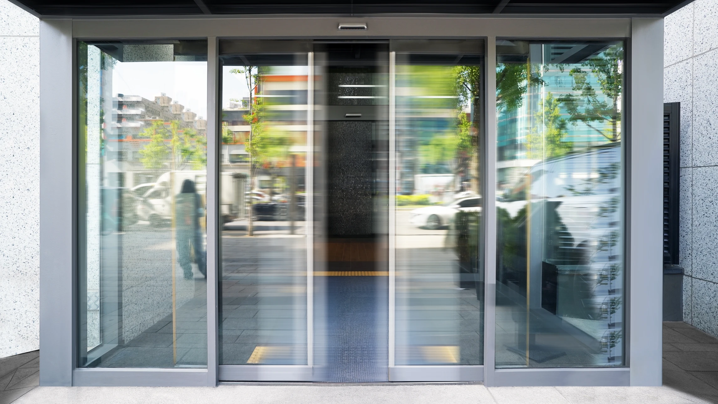 Entrée principale d'un immeuble de bureaux moderne avec porte automatique coulissante en verre, auvent en béton et sol carrelé